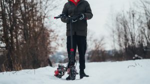 a man standing next to a scooter wearing snow pants, a winter jacket, and electric scooter riding gloves for winter