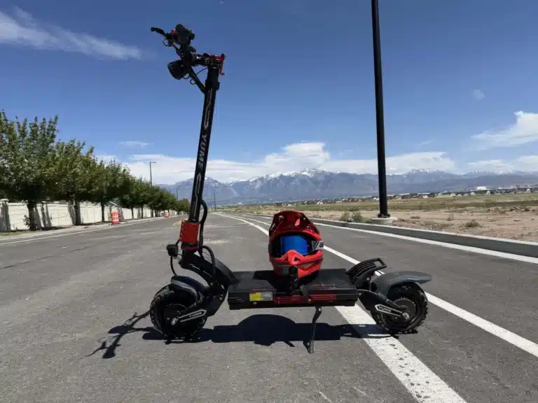 YUME Raptor 2 electric scooter parked on a road with a red full-face helmet on the deck and snow-capped mountains behind